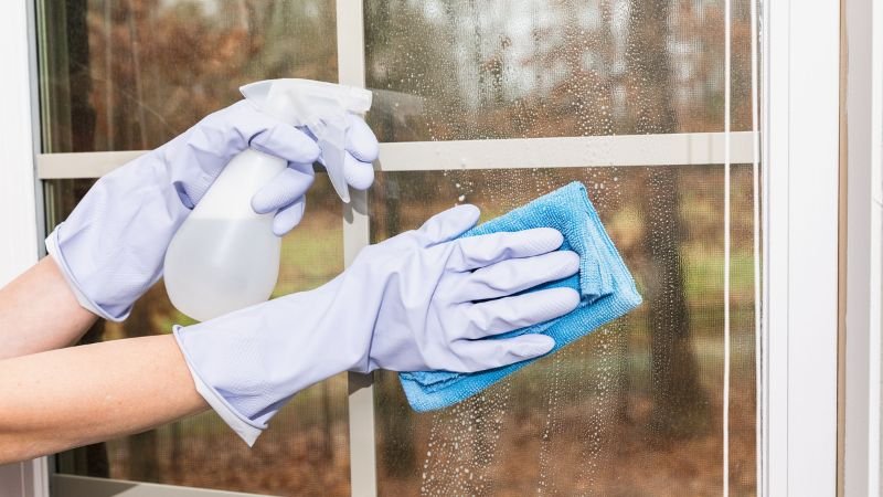 A person with gloves utilizes a blue sponge to clean a window, illustrating the work of a window cleaning service.
