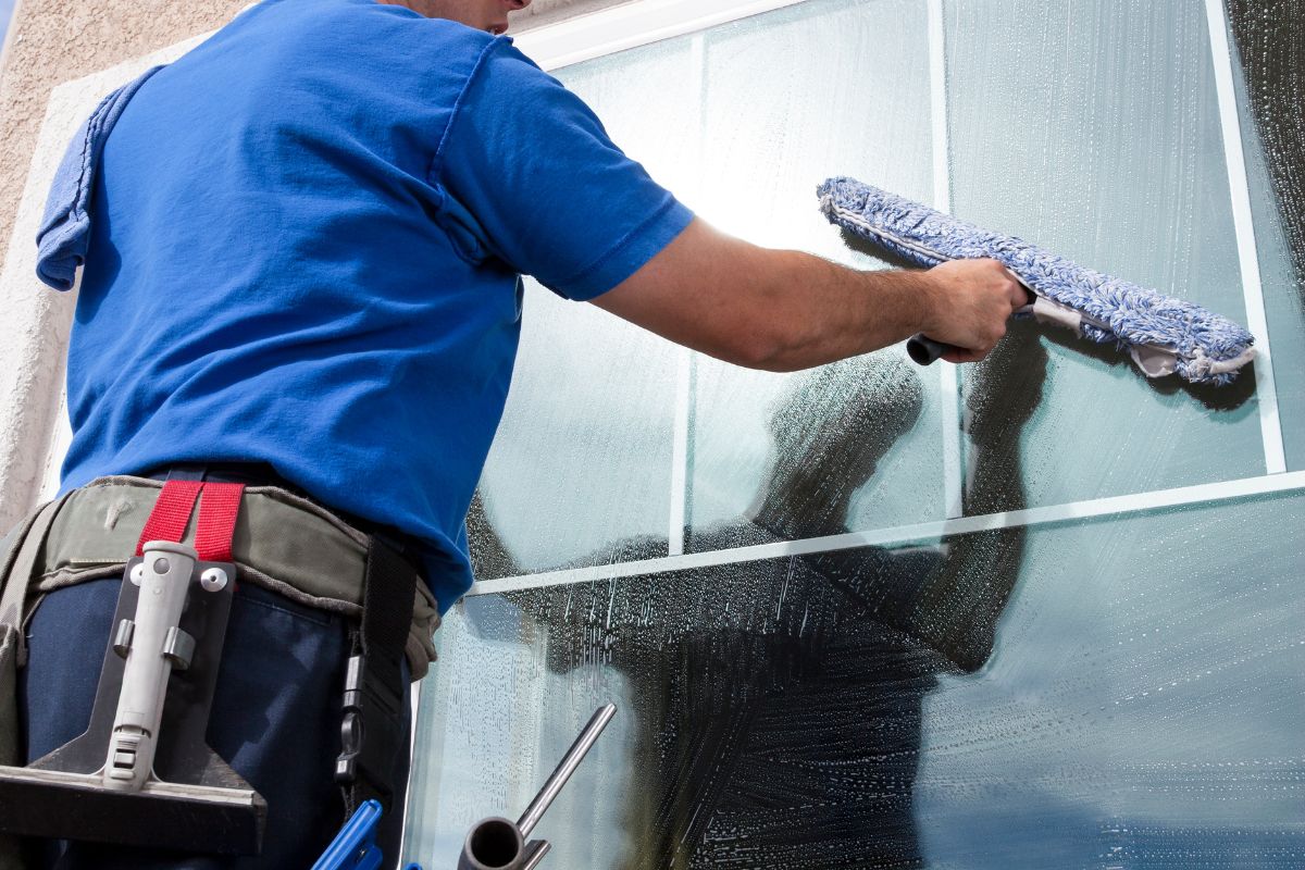 A man in a blue shirt uses a squeegee to clean a glass surface, ensuring a clear and polished finish.