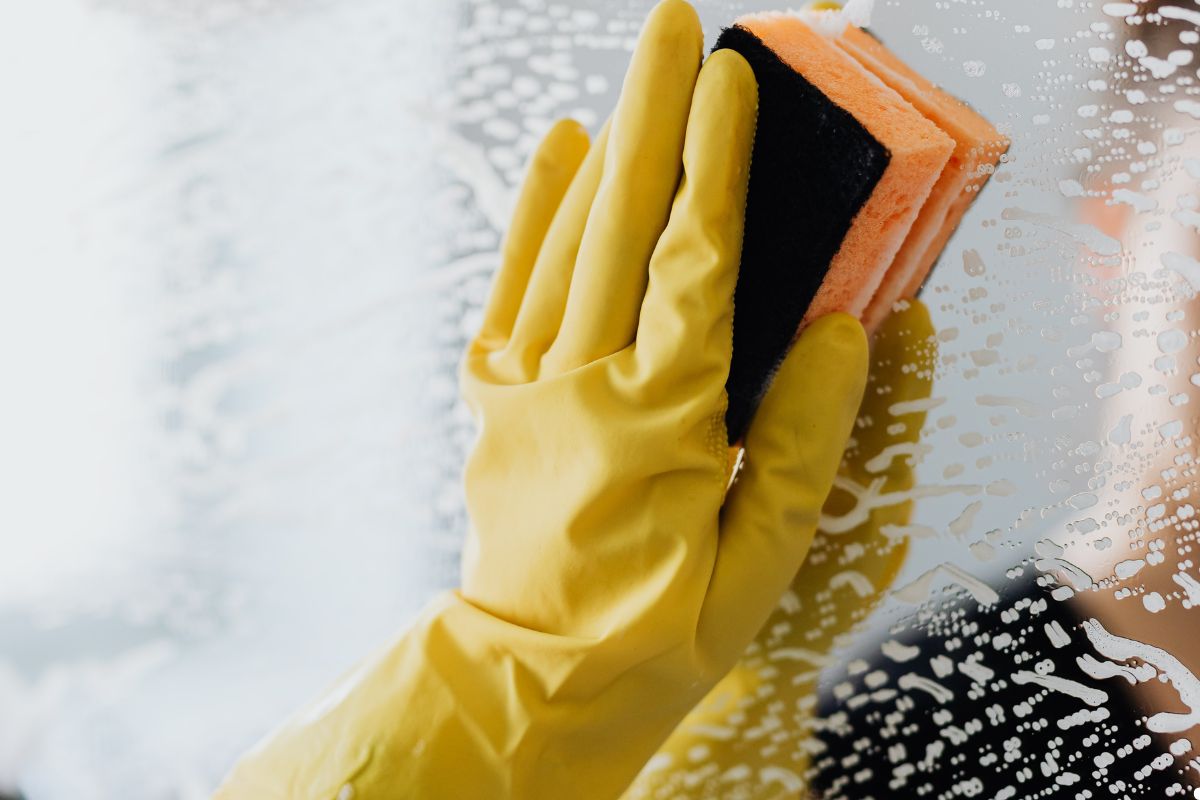 A person in yellow gloves is cleaning a window with a cloth, focusing on removing dirt and smudges.