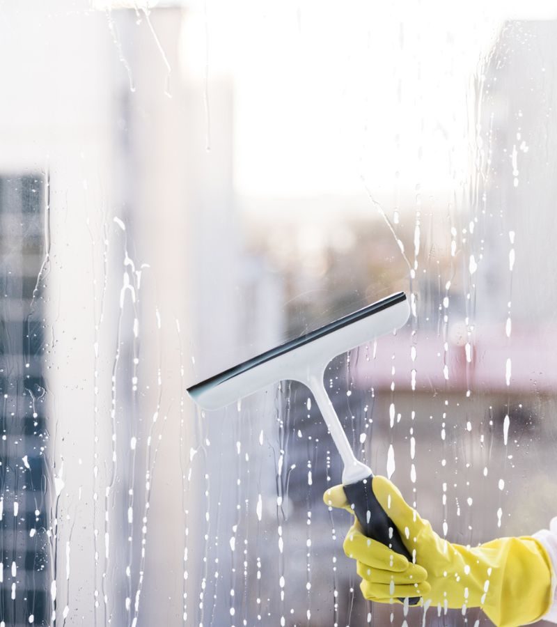 A person wearing yellow gloves meticulously cleans a window as part of a home window cleaning service.